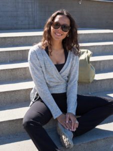 Woman sitting outside wearing a wrap-a-round top in grey melange color. Kvinna sitter utomhus klädd i en gråmelerad omlott top.