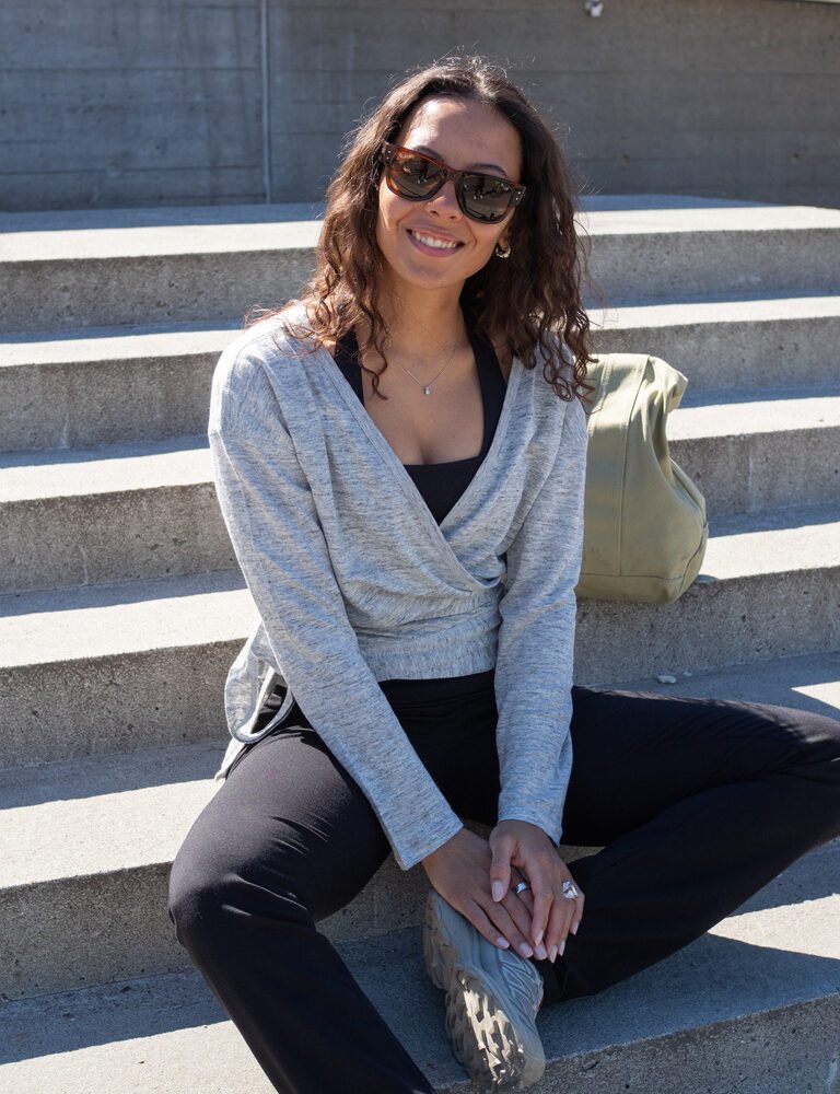 Woman sitting outside wearing a wrap-a-round top in grey melange color. Kvinna sitter utomhus klädd i en gråmelerad omlott top.
