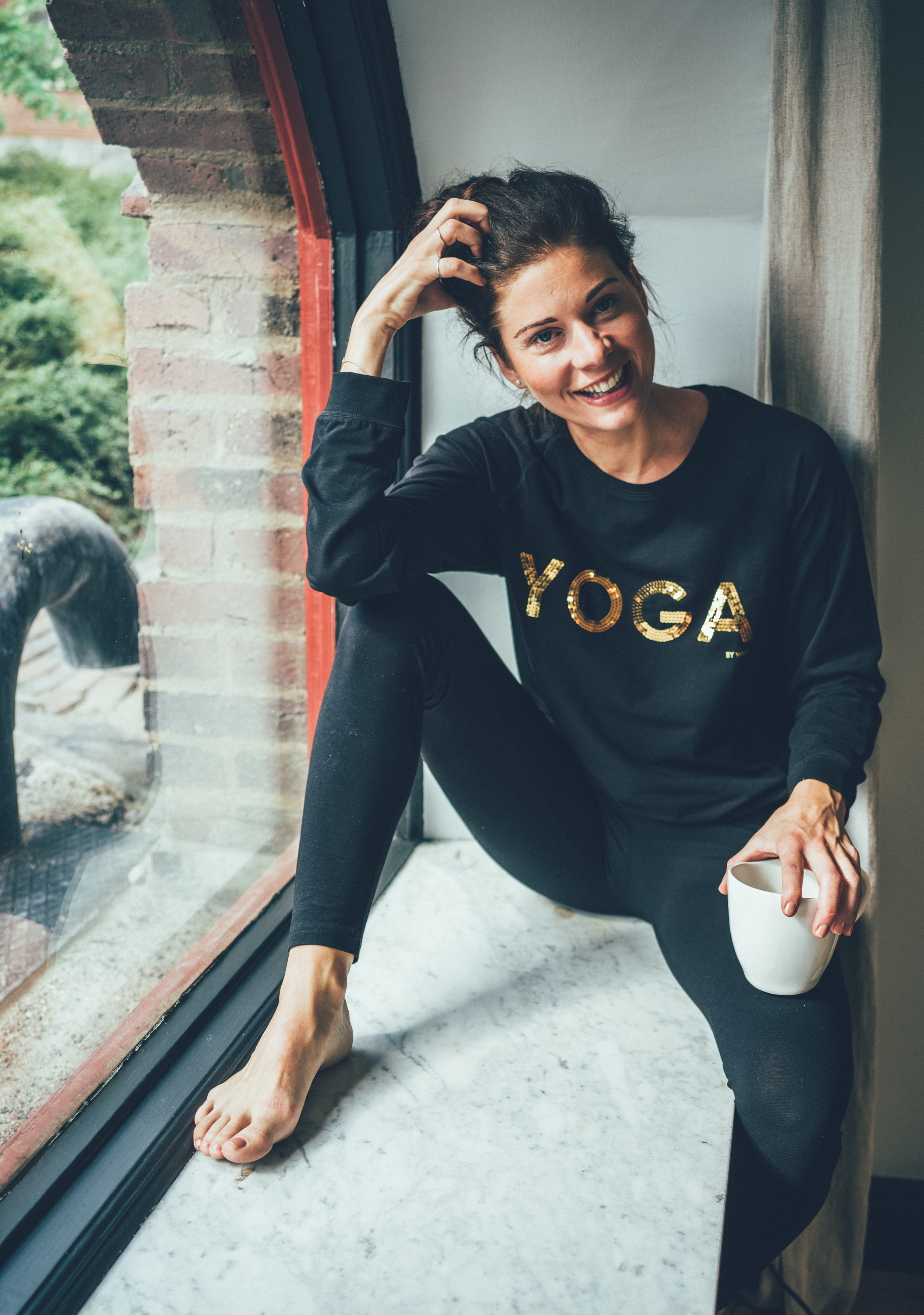 Model klädd i svarta yogabyxor och en yogatröja med texten YOGAS i guld.