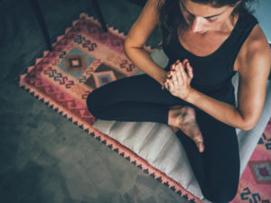 Girl meditates sitting on a zabuton and a pink kilim yoga mat.