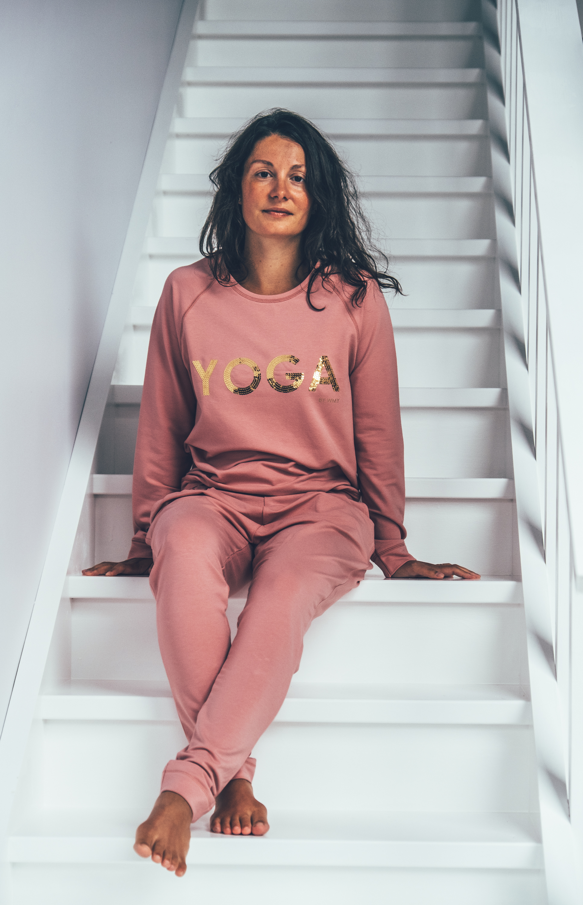 Modellen bär en rosa yogatröja med texten YOGA i guld.