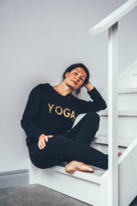 Model wearing a black yogasweater with the letters YOGA in gold.