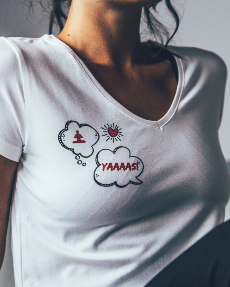 Model i vit t-shirt med yoga-tryck på höger bröst.