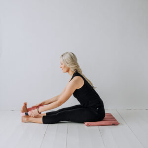 Yogi sittandes på en liten meditationsmatta användandes ett yoga bälte.