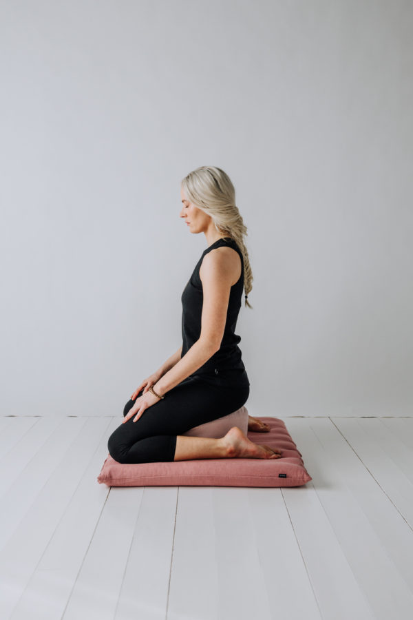 Mediterande Yogi sittandes på både en meditations kudde och en Zabuton, stor meditations matta, i linne