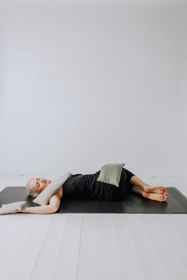 Yogi liggandes i en twist med tyngdkuddar på axeln, höften och handflatan.