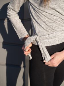 Woman making a knot at her wrap-a-round top in grey melange color. En kvinna knyter en knut på sin gråmelerad omlott top.
