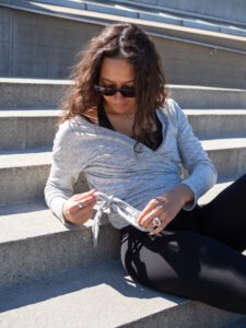 Woman sitting outside wearing a wrap-a-round top in grey melange color. Kvinna sitter utomhus klädd i en gråmelerad omlott top.