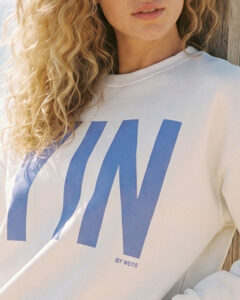 Woman wearing a white Sweatshirt with big letters at front in light blue color.